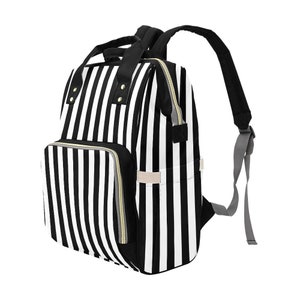 May include: Black and white striped backpack with a front pocket and gold-colored zippers. The backpack has two shoulder straps and a top handle. The bag is designed with a vertical stripe pattern.