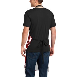 May include: A white apron with red splatters, worn by a person wearing a black t-shirt and blue jeans.