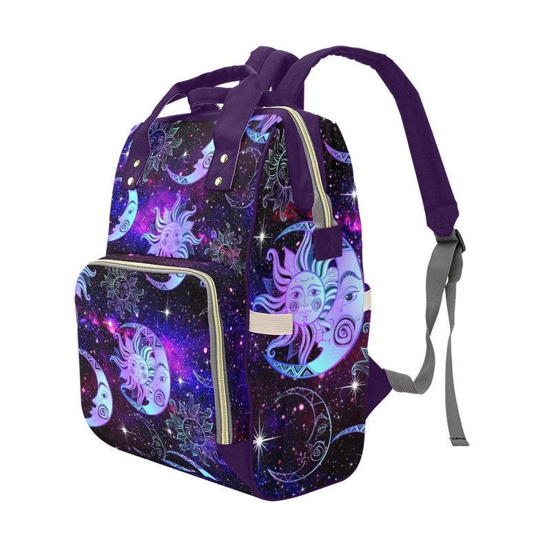 May include: Purple diaper bag with a galaxy print featuring moons and suns. The bag has a zippered front pocket and adjustable straps.
