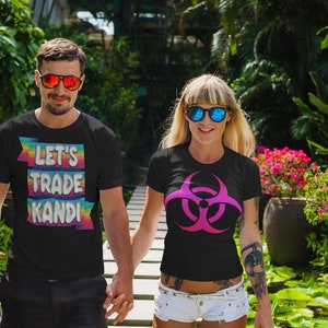 May include: Two people wearing black t-shirts with different designs. The person on the left is wearing a t-shirt with the text "Let's Trade Kandi" in rainbow colors. The person on the right is wearing a t-shirt with a pink biohazard symbol.
