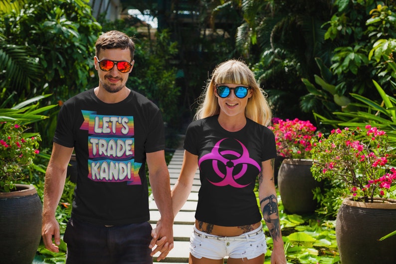 May include: Two people wearing black t-shirts with different designs. The person on the left is wearing a t-shirt with the text "Let's Trade Kandi" in rainbow colors. The person on the right is wearing a t-shirt with a pink biohazard symbol.