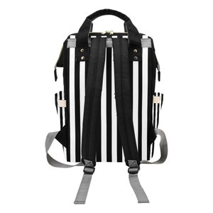 May include: A black and white striped backpack with adjustable shoulder straps and a top handle. The backpack has a zippered main compartment and side pockets. The straps are black, and the side straps are gray.