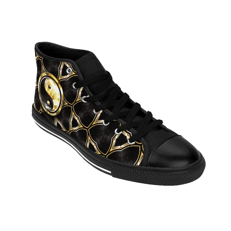 May include: Black high-top sneaker with a gold and black yin yang design. The shoe features a black toe cap, laces, and sole with a white stripe. The design includes a gold yin yang symbol and a gold geometric pattern.