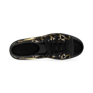 May include: Black high-top sneaker with a gold abstract design. The shoe features black laces, a black toe cap, and a black sole. The gold pattern covers the upper portion of the shoe.