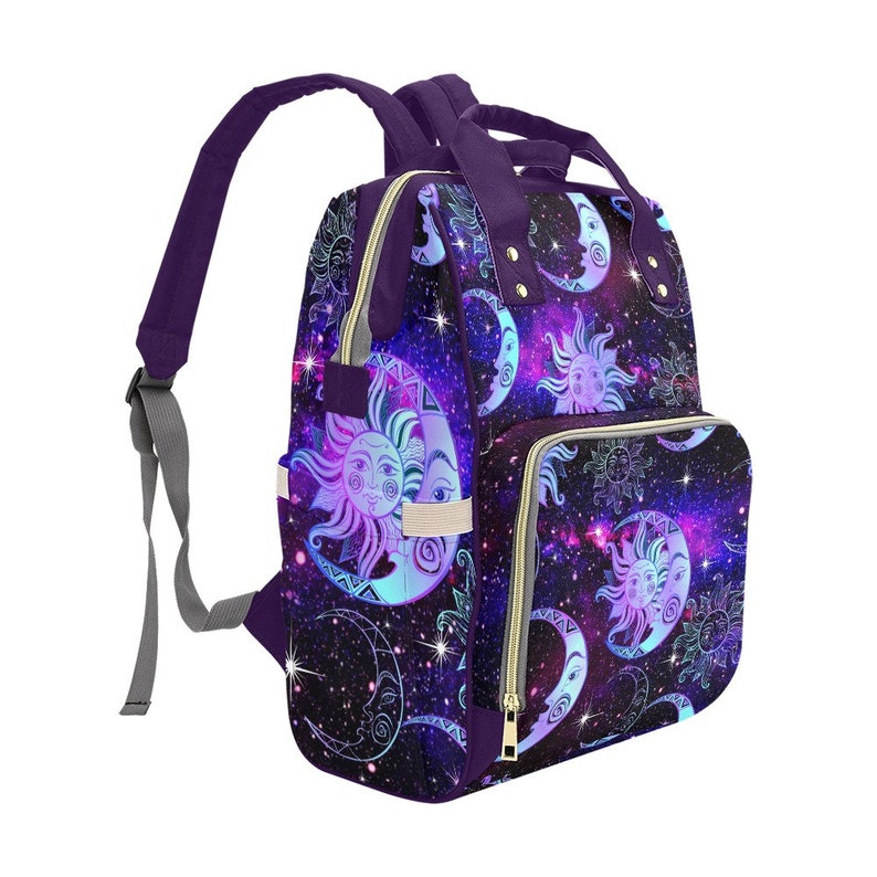 May include: Purple backpack with a galaxy print featuring suns and moons. The backpack has a zippered pocket on the front and adjustable straps.