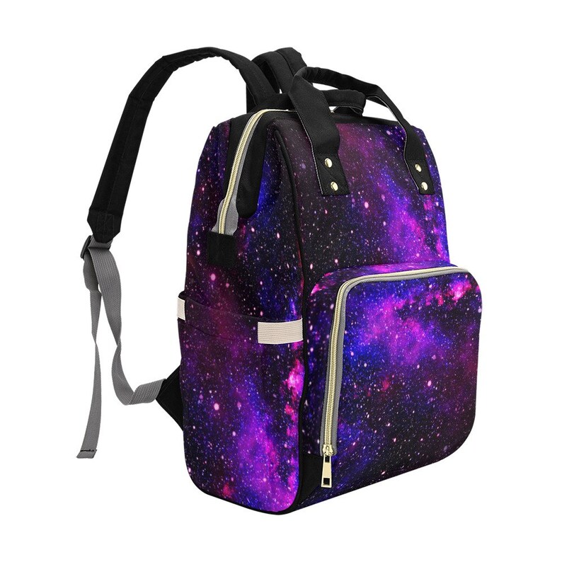Pode incluir: Uma mochila para fraldas preta e roxa com estampa de gal&aacute;xia, um bolso frontal grande e al&ccedil;as ajust&aacute;veis.