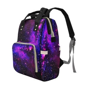 Pode incluir: Uma mochila preta para fraldas com estampa de gal&aacute;xia em cores roxa, rosa e azul. A mochila tem um bolso frontal com z&iacute;per e al&ccedil;as ajust&aacute;veis.