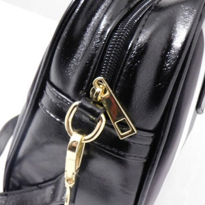 May include: Close-up of a black leather handbag with a gold zipper and a gold chain strap.