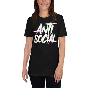 Puede incluir: Camiseta negra de manga corta con un gr&aacute;fico blanco que dice "ANTI SOCIAL" en una fuente con errores con acentos verdes y morados.