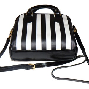 May include: Black and white striped handbag with a black leather bottom and a gold buckle on the strap.