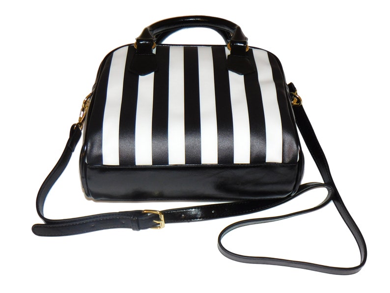May include: Black and white striped handbag with a black leather bottom and a gold buckle on the strap.