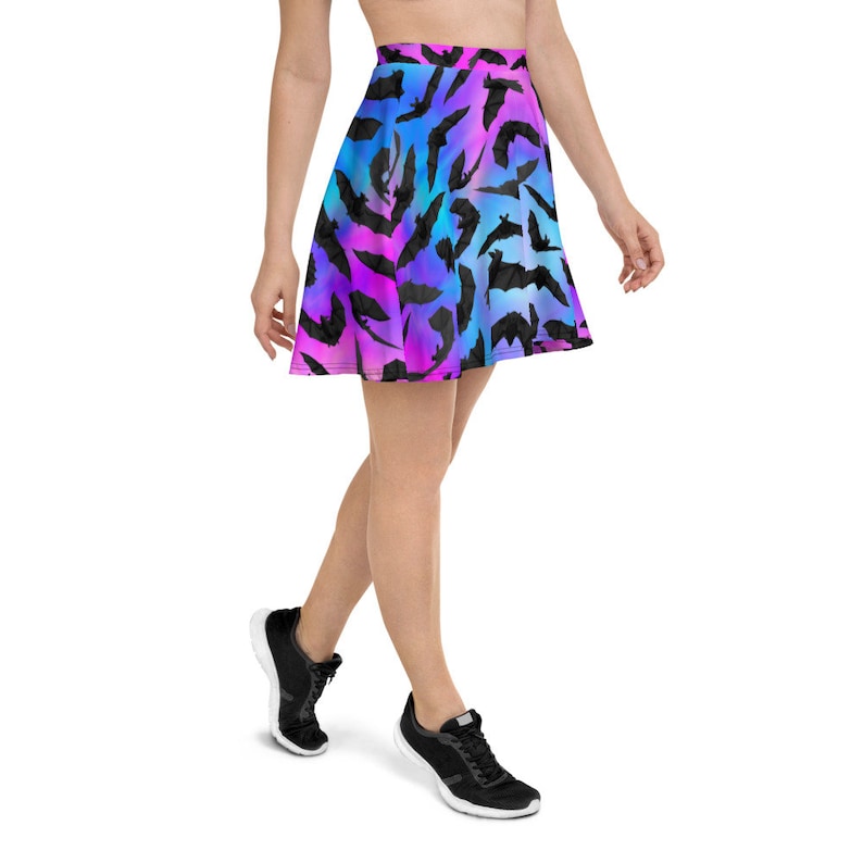 May include: A skater skirt with a colorful ombre pattern of pink, blue, and purple. The skirt is covered in a repeating pattern of black bat silhouettes.