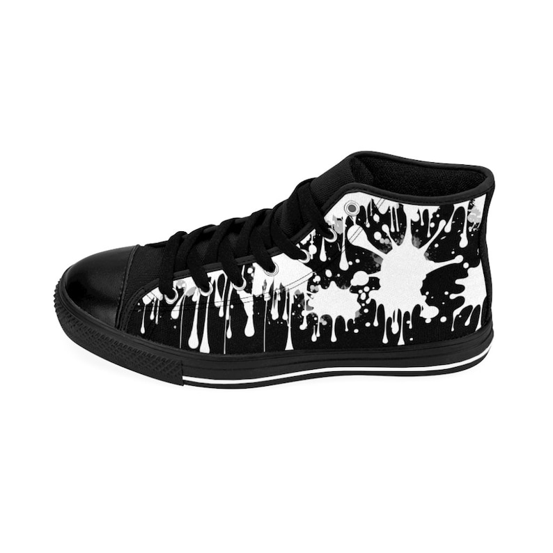 May include: Black high-top canvas sneakers with a white paint splatter design. The sneakers have a black rubber sole and white laces.