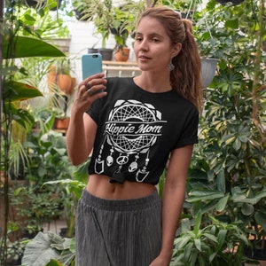 Może przedstawiać: Czarny T-shirt z białym wzorem łapacza sn&oacute;w i napisem "Hippie Mom". Koszulka jest zawiązana w talii, a modelka nosi szarą sp&oacute;dnicę.