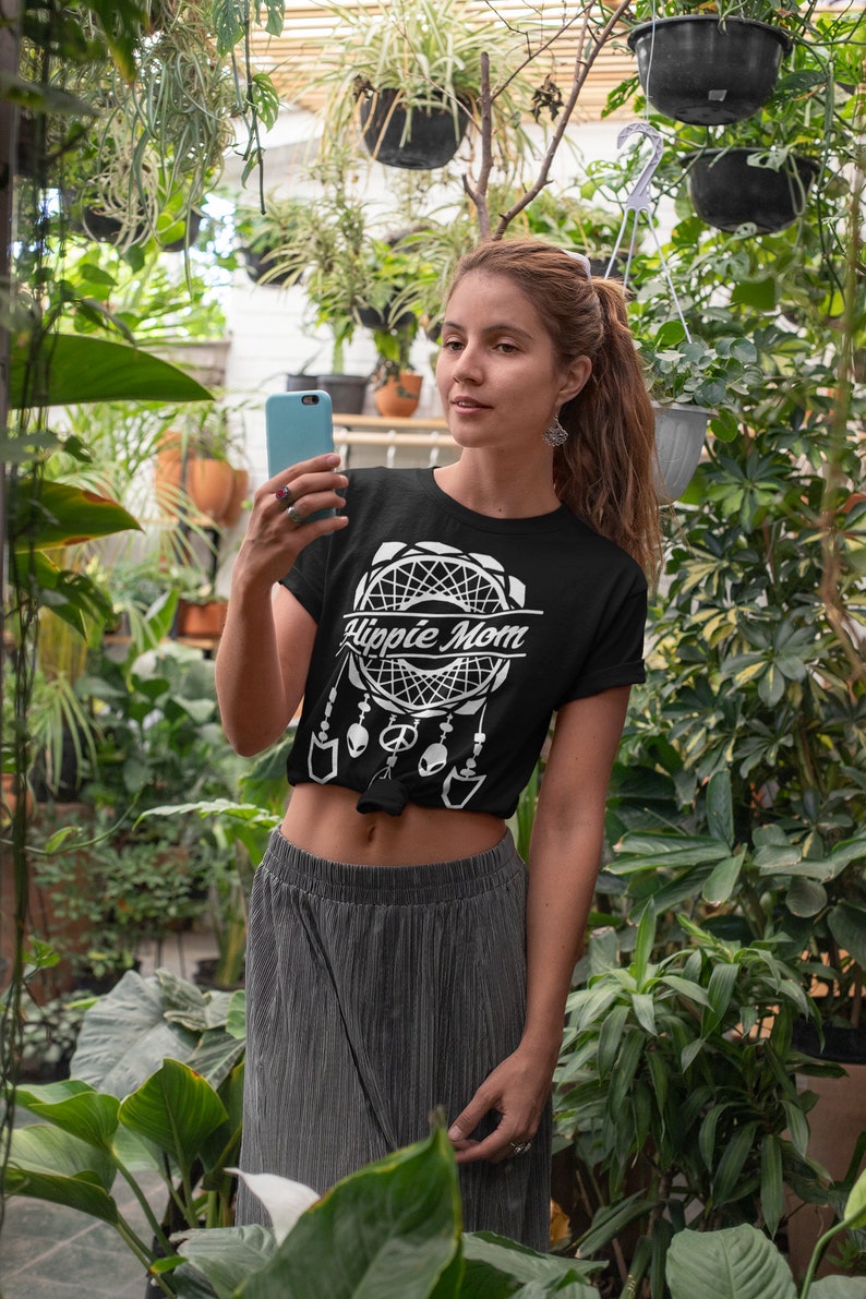 Może przedstawiać: Czarny T-shirt z białym wzorem łapacza sn&oacute;w i napisem "Hippie Mom". Koszulka jest zawiązana w talii, a modelka nosi szarą sp&oacute;dnicę.