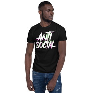 Puede incluir: Una camiseta negra con un gr&aacute;fico blanco que dice "ANTI SOCIAL" en una fuente con efecto glitch con acentos rosas y verdes.