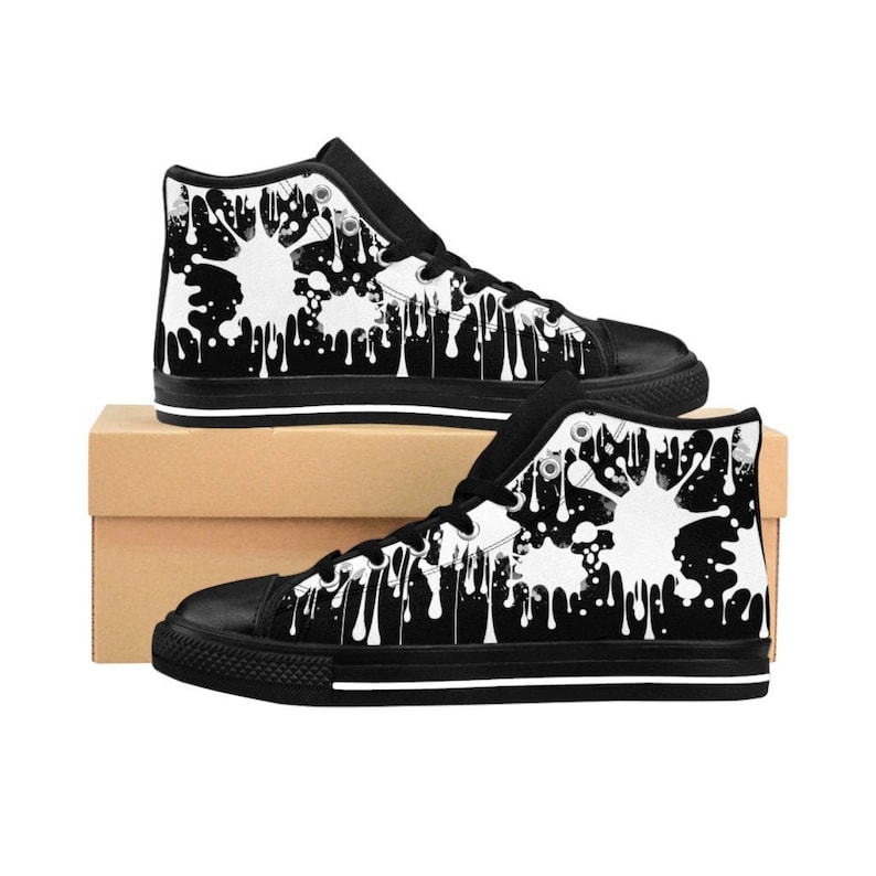 May include: Black and white high-top canvas shoes with a white paint splatter design. The shoes have a black sole and white laces.