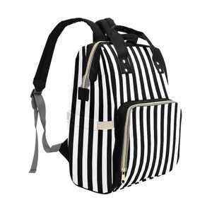 May include: A black and white striped backpack with a front pocket and gold zippers. The backpack has black shoulder straps and a top handle. The bag is designed with vertical stripes.