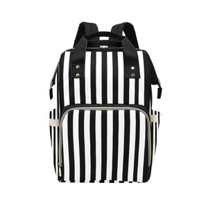 May include: Black and white striped backpack with multiple compartments and pockets. The bag has a top handle and adjustable shoulder straps. The exterior features a bold vertical stripe pattern, with gold-colored zippers and accents.