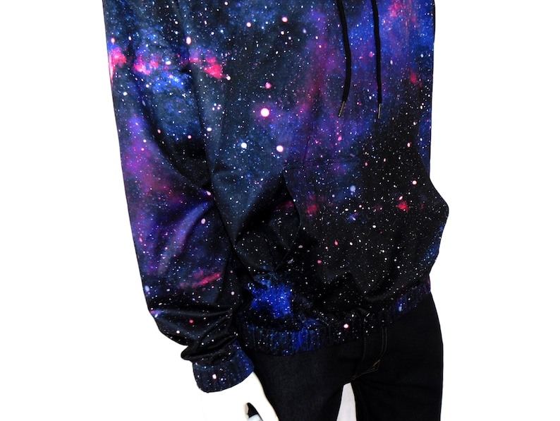 May include: A black hoodie with a galaxy print featuring shades of blue, pink, and white. The hoodie has a drawstring hood and a kangaroo pocket.