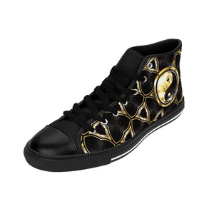 May include: Black high-top sneakers with a black rubber sole and black laces. The side of the shoe features a gold and black geometric pattern with a gold yin-yang symbol. The shoe is made of canvas.