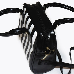 May include: A black and white striped handbag with a black leather handle and a long black strap.