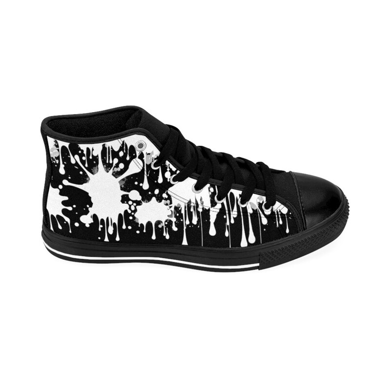 May include: Black high-top canvas sneakers with a white paint splatter design. The sneakers have black laces and a white rubber sole.