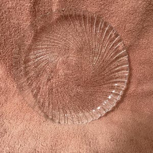 May include: A clear glass plate with a spiral design. The plate has a textured surface and a scalloped edge. The plate is round and appears to be made of glass.