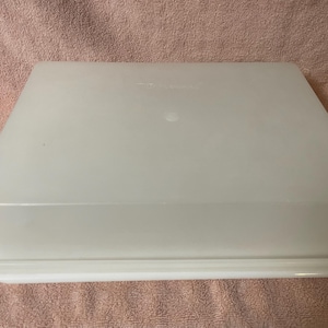 May include: A rectangular, semi-translucent white plastic storage container with a matching lid. The container features a flat top surface and a slightly wider base rim, providing a secure fit for the lid. The material is smooth and opaque.