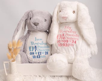 May include: Two plush stuffed rabbits, one grey and one white, featuring embroidered birth details. The grey rabbit displays the name Luca Brownless, 8 Pounds 7 Ounces, 08 12 21, 11:12 am. The white rabbit displays Lily Brownless, 8 Pounds 14 Ounces, 10 09 24, 13:03 pm.
