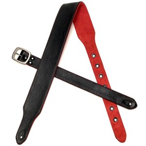 May include: Black leather guitar strap with red stitching and a silver buckle. The strap has multiple adjustment holes.