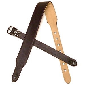 May include: A brown leather guitar strap with a silver buckle and adjustable length. The strap has multiple holes for adjusting the length.