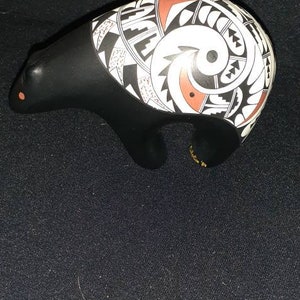 May include: Black ceramic bear figurine with white and red geometric patterns. The bear is standing on all fours and has a stylized design.