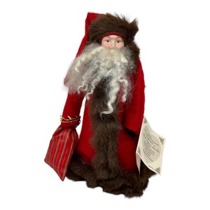 May include: A red felt Santa Claus doll with a white beard and brown fur trim. The doll is holding a red and gold plaid bag. The doll has a tag that says "The Price Is Santa".