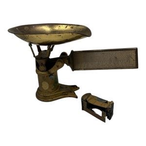 May include: An antique brass scale with a curved tray, a rectangular weight indicator, and a separate weight holder. The scale has a worn, vintage appearance, with signs of age and use. The scale is likely used for measuring weight.