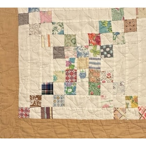 May include: A patchwork quilt featuring a central grid of small, multi-colored fabric squares in various floral, plaid, and geometric patterns. The quilt is bordered by a solid tan fabric and features overall quilted stitching in a curved pattern.