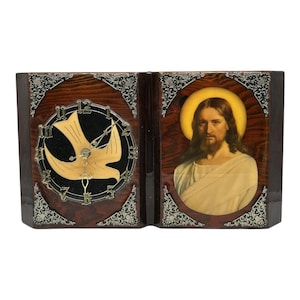 Puede incluir: Un reloj de madera con forma de libro con una paloma y una esfera de reloj en un lado y un retrato de Jesús en el otro. La esfera del reloj tiene números romanos y una paloma dorada.