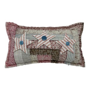 May include: A rectangular patchwork pillow with three red and white striped stars with blue buttons in the center. The pillow is made of various fabrics in shades of brown, pink, and white.