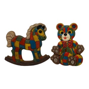 May include: Two colorful, patchwork-style wall decorations: a rocking horse and a teddy bear. The horse is brown with a yellow mane and tail, and the bear is brown with a red bow tie.