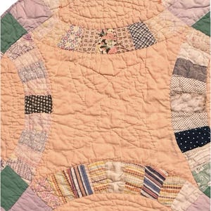 Puede incluir: Primer plano de un edredón vintage con un centro color melocotón y bordes de patchwork coloridos. El edredón presenta un diseño de doble anillo de boda con varias telas estampadas en tonos de rosa, verde, azul y crema. El edredón tiene una textura acolchada.