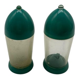 May include: Two vintage salt and pepper shakers. Each shaker has a green, rounded top with a clear glass knob. The lower half of one shaker is clear, while the other is silver. Both have a green base.