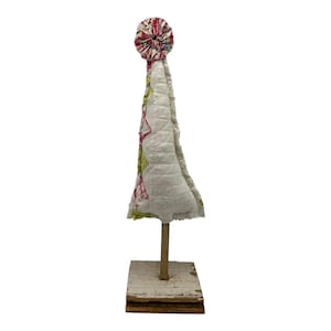 May include: A small white fabric Christmas tree with a pink and green patterned top, standing on a wooden base.