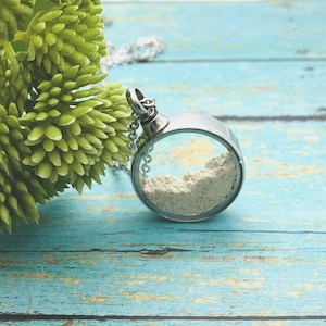 May include: A silver necklace with a round pendant containing a white powder. The pendant is open on one side, revealing the powder inside.