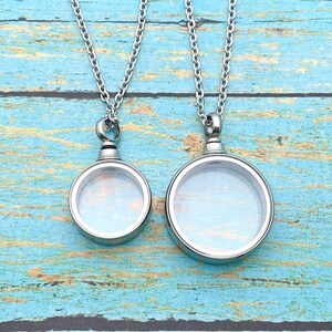 May include: Two silver chain necklaces with round glass locket pendants. The lockets are open and have a clear glass interior.