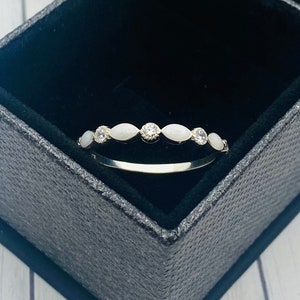May include: A silver ring with a row of oval-shaped white stones set in a delicate band. The ring is displayed in a black velvet ring box.