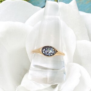 May include: A gold ring with a round iridescent stone set in a bezel setting.