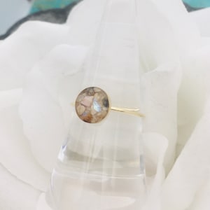 May include: A gold ring with a round, iridescent stone set in the center. The stone is made of crushed opal and other materials.