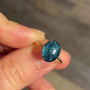 May include: A gold ring with a teal blue oval-shaped stone filled with glitter.