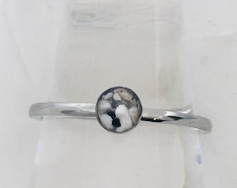 May include: A silver ring with a white and black speckled stone.