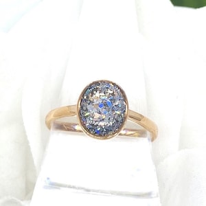 May include: A gold ring with a large oval-shaped clear stone set in the center. The stone is covered in iridescent glitter.